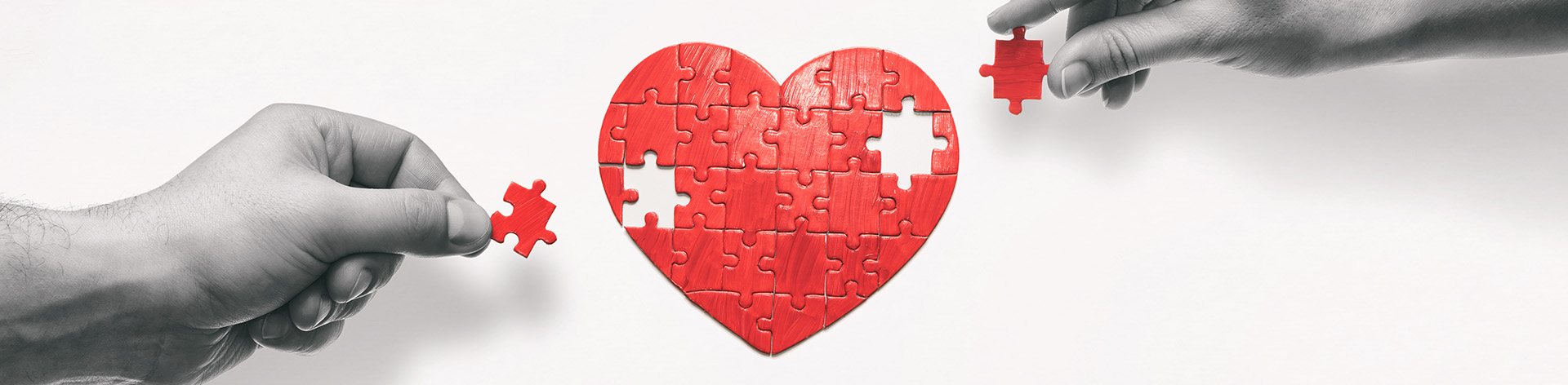 Hands place the last of two puzzle pieces to form a red heart.